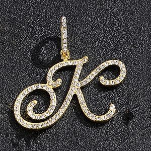 Close-up of gold-plated iced-out letter K pendant with white rhinestones on black background