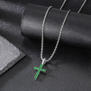 Macro detail of silver cross pendant with sparkling green zircons on a twisted rope chain