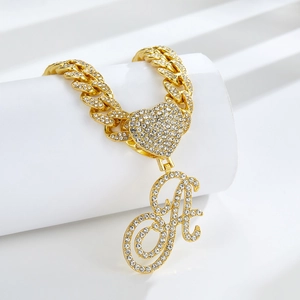 Détail d'un collier à maille gourmette dorée avec cœur en strass et pendentif A