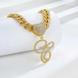 Détail d'une chaîne cubaine dorée avec fermoir coeur et pendentif lettre G en diamants
