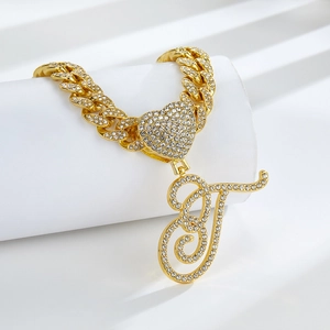 Détail de la chaîne cubaine dorée avec un cœur serti de diamants et un pendentif lettre T