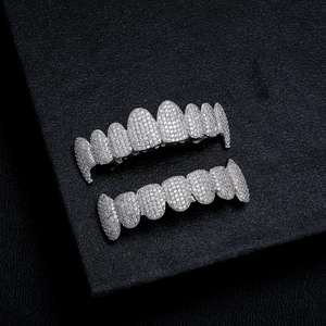 Macro shot of silver hip hop grillz with white zircon pavé setting on black leather background