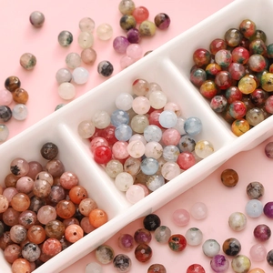 Faceted natural stone beads in assorted colors displayed on a white ceramic tray