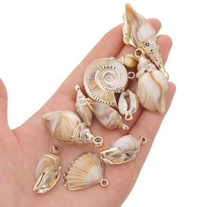 Handheld view of assorted gold shell pendants including conch and nautilus for DIY jewelry