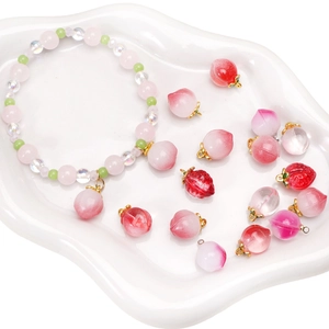 Pink peach and strawberry glass charms with beaded bracelet on a white ceramic plate