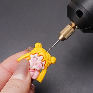 Primo piano di un mini trapano elettrico che fora un accessorio in resina gialla