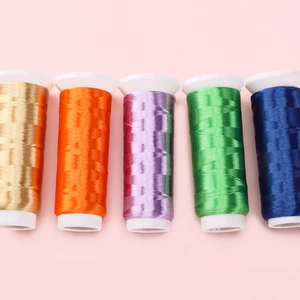 Nahaufnahme von fünf bunten, glänzenden Stickgarnspulen für DIY-Handwerk auf rosa Grund