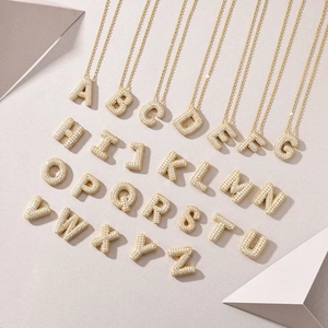 Close-up of 26 gold letter pendants with sparkling moissanite on textured background