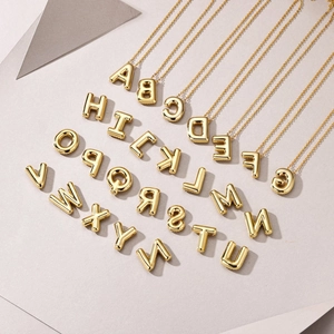 Flat lay of 26 3D bubble letter necklaces in gold plating over a beige background