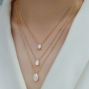 Three-layer gold necklace with pear-cut moissanite pendants worn on a white suit