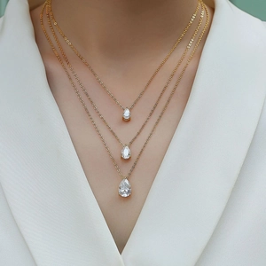 Three-layer gold necklace set featuring teardrop pendants on a female model with white suit