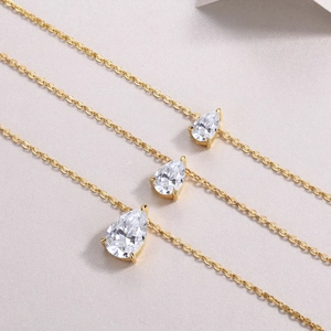 Macro shot of three teardrop shaped moissanite pendants in gold finish with thin chains
