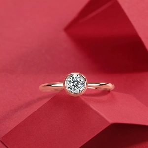 Dettaglio macro di un anello con diamante a castone in oro rosa su uno sfondo rosso artistico