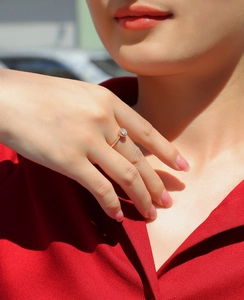 Dettaglio di un anello solitario in oro rosa con montatura a castone su sfondo rosso