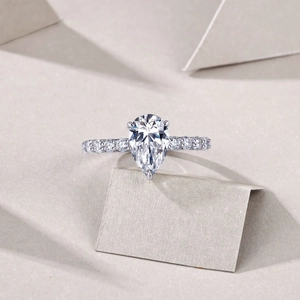 Gros plan d'une bague moissanite taille poire avec anneau pavé sur fond minimaliste