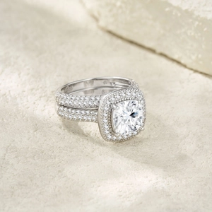 Macro shot of cushion-cut silver bridal set rings with pavé diamonds on textured stone