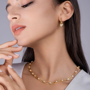 Gros plan du collier maillons trombone dorés avec pierres pavées et boucles d'oreilles cœur