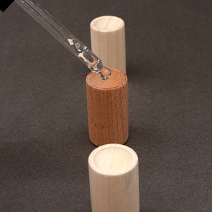 Macro shot showing essential oil dropping onto a cylindrical wooden diffuser base