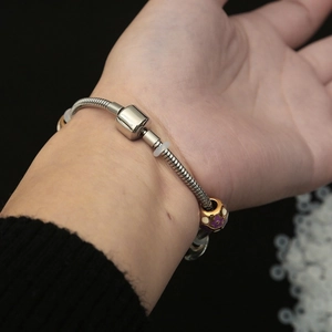 Silbernes Schlangenarmband mit violetter Blumenperle und Fassverschluss am Handgelenk