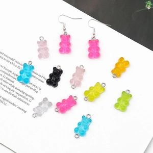 Pendentifs et boucles d'oreilles oursons en résine colorée sur un support papier blanc