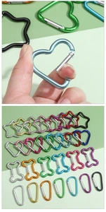 Close-up of heart-shaped aluminum carabiner being opened next to colorful multi-shape hooks