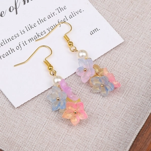 Detail of handmade colorful floral resin earrings with pearls and gold hooks on beige fabric