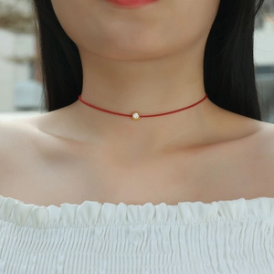 Dettaglio del girocollo a cordoncino rosso con pendente dorato e moissanite indossato