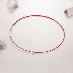 Dettaglio macro della collana a cordino rosso con perla dorata e zircone lucente
