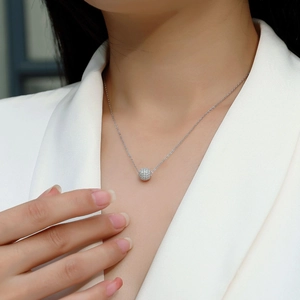Detail of a sparkling pavé crystal ball pendant on a 925 silver necklace worn by a model