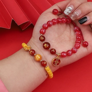 Detalle de pulseras de ágata roja con dijes dorados sobre fondo festivo rojo