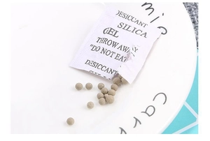 Close-up of silica gel desiccant beads and white non-woven packet on a ceramic plate
