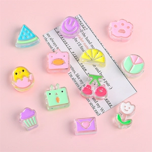 Assorted colorful acrylic DIY charms with cute animal and fruit shapes on a pink background