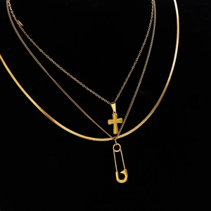 Three-layer gold necklace set with cross and safety pin pendants on a black background