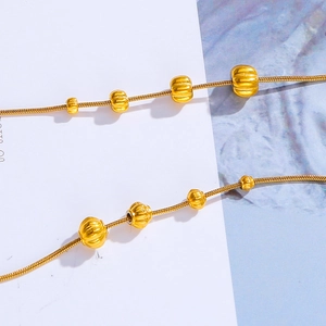 Macro shot of golden pumpkin bead charms and sleek snake chain necklace texture