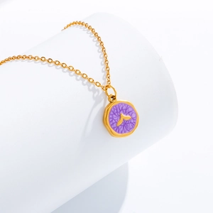 Detail view of a gold-plated necklace featuring a purple round whale tail charm on a white stand