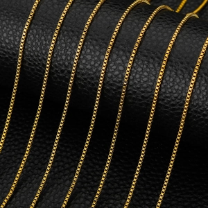 Macro detail of 1.5mm gold stainless steel box chains on black leather background