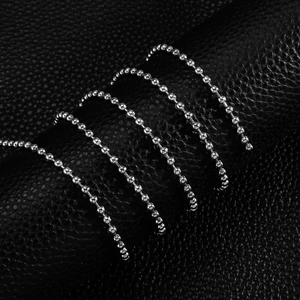 Polished stainless steel ball chain necklace spiraled on a black leather background