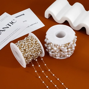 Detail of golden stainless steel chains with round and heart pearls on white spools