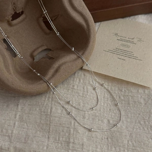 Minimalist S925 silver double-layered snake chain necklace with beads displayed on a rustic stand