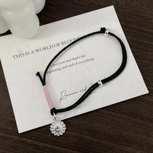 Detail of hand-woven black cord bracelet with silver smiley sunflower charm and pink accents