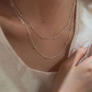 Close-up of double layer silver beaded snake chain necklace worn on white sweater