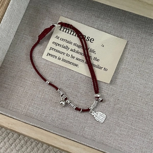 Close-up of handmade red braided silver bracelet with engraved charm and bell detail