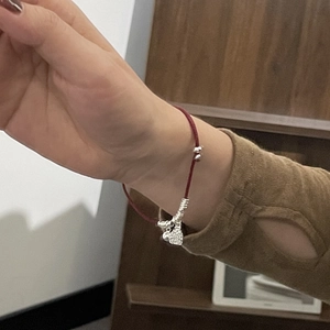 Detail view of a red woven S925 sterling silver bracelet on wrist with elegant metal charms
