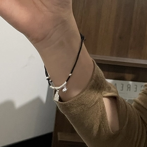 Detail of s925 silver charms on a minimalist black hand-woven bracelet for women