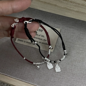 Macro detail of hand-woven red and black bracelets with silver Fu character charm