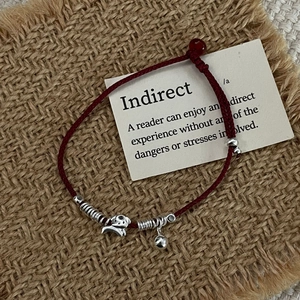 Detail of red hand-woven rope bracelet with 925 silver puppy charm and bell on rustic linen