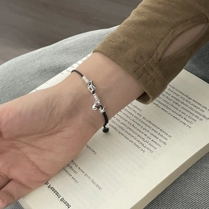Detail of hand-woven black cord bracelet with silver puppy bell charms on a wrist