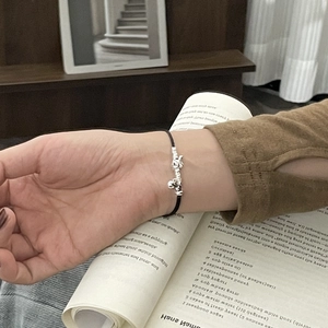 Close-up of a black woven rope bracelet with 925 silver puppy charm and small bell