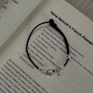 Close-up of adjustable black woven bracelet with silver puppy charm and bell on book