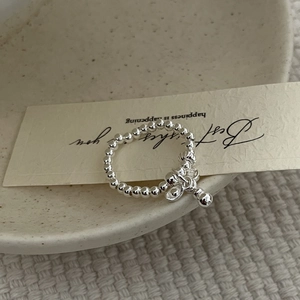 Detail of a minimalist silver beaded ring with a small charm on a textured tray